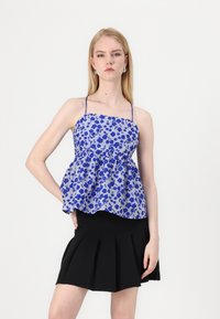 Blauw bloemenpatroon peplum top met dunne banden, gecombineerd met een zwarte plissérok. Gladde stof, aansluitend bij de taille, uitlopend aan de onderkant.