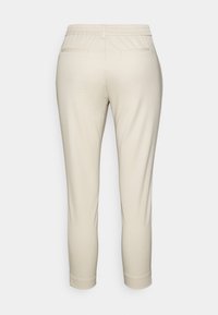 Beżowe spodnie z elastycznym pasem, slim fit, dwoma tylnymi kieszeniami oraz gładkim, teksturowanym materiałem. Dół jest lekko zwężany.