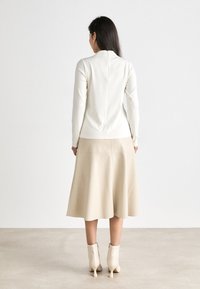En kremfarget tettsittende topp med ståkrage og bakseen, kombinert med et beigefarget svevende skjørt. Bært med lysebeige høye ankelstøvler.