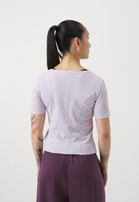 T-shirt lilas à rayures avec des manches courtes, dotée d'un col rond et d'une coupe ajustée. Portée avec un pantalon violet, montrant une texture lisse.