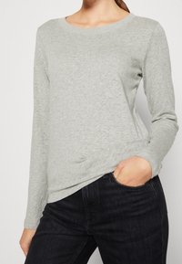 Lichtgrijze longsleeve t-shirt van zachte stof, met een ronde halslijn en zijsplitdetails, gecombineerd met donkere spijkerbroeken.