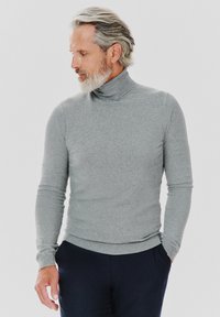 Szary sweter z golfem wykonany z delikatnej dzianiny, z długimi rękawami i przylegającym krojem. W połączeniu z ciemnymi spodniami. Minimalistyczny design.