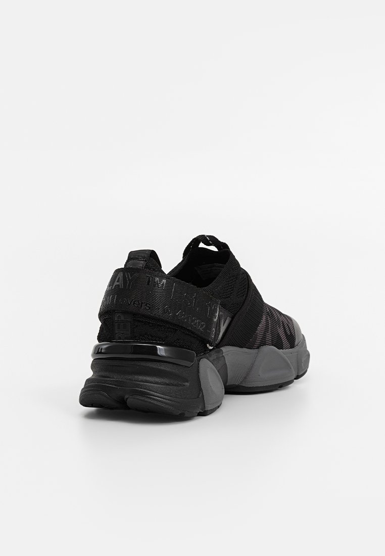 Baskets de sport noires avec une tige en mesh texturé, une semelle épaisse et un accent brillant au niveau du talon. Présente un design à motifs sur le côté et un marquage à l'arrière.