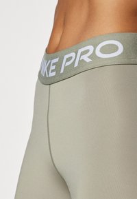 Nike Pro tajice u svijetlo maslinastoj zelenoj boji, s širokim, teksturiranim pojasom s bijelim "NIKE PRO" logotipom i glatkim, rastezljivim materijalom.