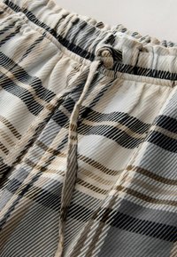 Plaid patterned shorts with an elastic waistband and drawstring. Colors include beige, black, and gray with ribbed texture.