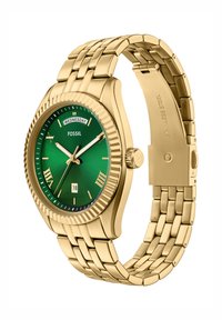 Guld rostfritt stål klocka med grön urtavla, romerska siffersmarkeringar, datumsdisplay och ett guld länkarmband. Har en strukturerad bezel.