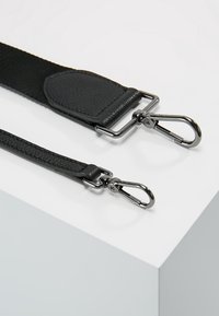 Sangles de sac noires réglables avec fermoirs pivotants en métal, une plus large avec détail en cuir et une plus étroite avec finition texturée.