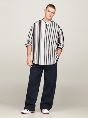 Striped skjorte med høy krage, med blå, hvite og oransje striper; sammen med marineblå bukser og hvite sneakers med burgunder detaljer.