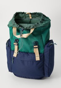 Zaino con una parte superiore verde e una parte inferiore blu navy, dotato di spallacci regolabili beige e tasche laterali. Realizzato in tessuto resistente e con chiusura a coulisse.