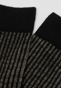 Stricksocken mit einem schwarzen Rippenmuster, das mit metallischen silbernen Fäden durchzogen ist, um Textur und Kontrast hinzuzufügen.