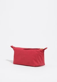 Saco de tela suave y rojo con forma rectangular, cierre de cremallera y una pequeña asa. Superficie texturizada con un acabado mate.