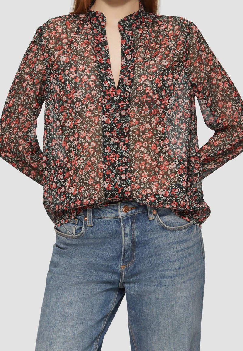 Blouse florale noire, avec un col en V, ornée de petites fleurs rouges et blanches, à manches longues et à coupe décontractée.