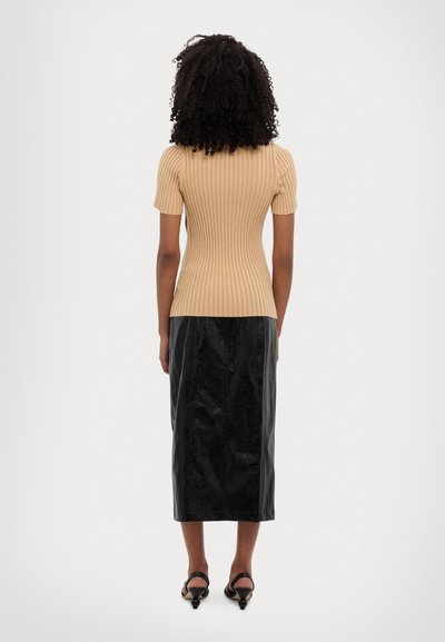 Beige geripptes kurzärmliges Oberteil kombiniert mit einem schwarzen, glänzenden knielangen Rock, der eine figurbetonte Silhouette und minimale Details aufweist.