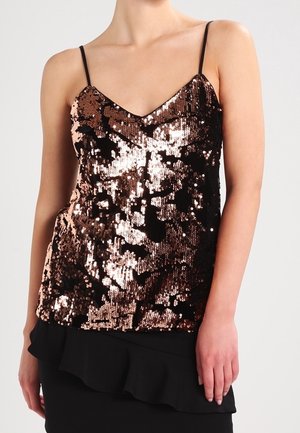 Kvinde iført en ærmeløs bronze- og sort paliet-top med tynde stropper og V-udskæring, kombineret med et sort rynket skørt.