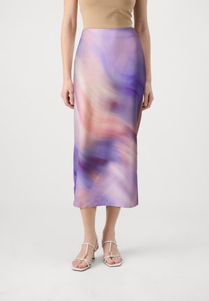 Kvinde iført en højttaljet, lilla og pink midi-nederdel med abstrakt print, beige remsandaler og en ærmeløs beige top.