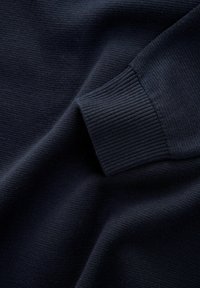 Mörk marinblå stickad tröja med ärm och ribbad manschett, visad mot en texturerad tygbakgrund.