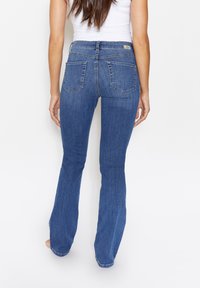 Jeans acampanados de denim azul oscuro ajustados a la cintura alta, con dos bolsillos traseros y una etiqueta de marca cosida en la cintura.