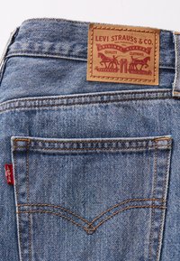 Modré džíny z denimu s koženou nášivkou "LEVI STRAUSS & CO." a oranžovým prošíváním. Obsahuje červenou visačku na levé kapse.