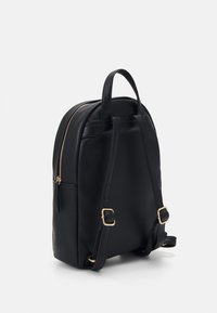 Mochila de cuero negra con forma redondeada, cremalleras doradas, correas ajustables y un bolsillo frontal. Textura suave en todo.