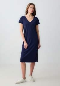 Vestito blu navy a lunghezza ginocchio con scollatura a V e maniche corte, con una spacco laterale. Realizzato in un tessuto morbido e liscio, abbinato a sneakers bianche.