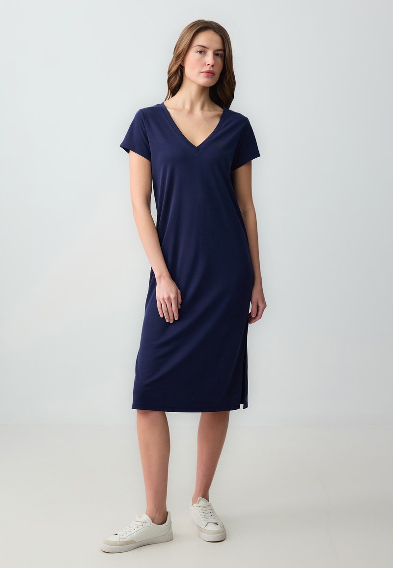 Vestito blu navy a lunghezza ginocchio con scollatura a V e maniche corte, con una spacco laterale. Realizzato in un tessuto morbido e liscio, abbinato a sneakers bianche.