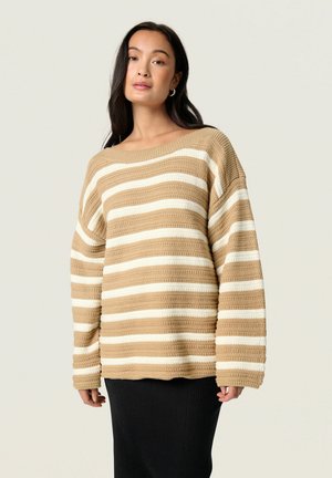 Beige og creme stribet sweater med en løs pasform, struktureret strikstof, bred bådudskæring og lange ærmer. Båret med en sort ribbet nederdel.