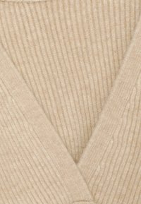 Beige ribbad stickad cardigan med V-ringning och omslagen design, som betonar mjuk textur och enkla, rena linjer.