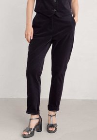 Črne kordurojske hlače s sproščenim krojem, z stranskimi žepi in zavihanimi robovi. Ujemajoče se z kovinskimi sandali na peto.