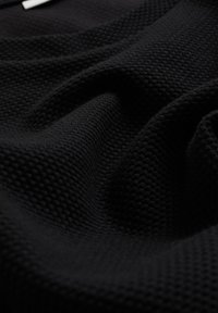 Material textil negru cu o textură ondulată, având un model de tip wafel; pliuri moi și maleabile. Suprafață netedă cu un luciu subtil și fără accente vizibile.