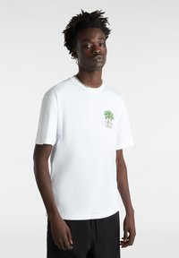 Hvid T-shirt med korte ærmer, der har et lille grønt palmetræ-graphic og "VANS" tekst på venstre brystlommeområde. Fremstillet af bomuldsmateriale.