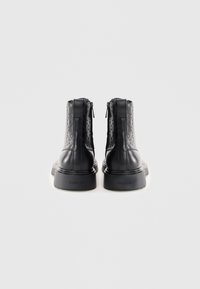 Botas de tobillo negras con parte superior texturizada, secciones de cuero liso, cremalleras traseras y suela gruesa, con un logotipo grabado en el lateral.