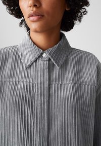 Grijze corduroy overhemd met een kraag, met een verticale ribbeltextuur en een knoopsluiting bij de kraag.