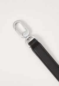 Pulseira de couro preto com um prendedor metálico prateado brilhante. A pulseira é lisa, com costuras visíveis que detalham o design.