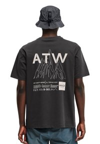 Sort bomulds T-shirt med et bjergdesign, stort "ATW" bogstaver og trykte tekstdetaljer på ryggen. Kombiner med en grå bøttehat.