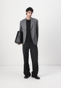 Gray pinstripe blazer over a black shirt, paired with dark wide-leg jeans and shiny black shoes; model holding a black tote bag.