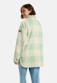 Groene en crème geruite fleecejas met een kraag, textuurstof en een merkpatch op de linker mouw. Loose fit, knoopsluiting.