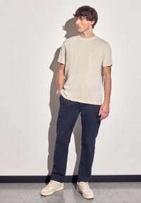 Světle béžová košile s krátkým rukávem a námořnické cargo kalhoty. Béžové tenisky s texturovaným povrchem. Hladká látka, volný střih a jednoduchý design.