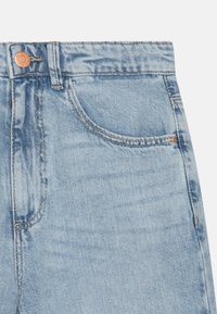 Jeans de mezclilla azul claro con una textura ligeramente deslavada, presentan un bolsillo frontal y un detalle de botón en tono cobre en la cintura.