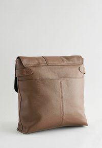 Sac en cuir marron avec une finition texturée, doté d'une fermeture à rabat et de sangles latérales ajustables. Forme douce et rectangulaire avec un design minimaliste.