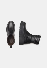 Bottines noires en cuir avec une semelle épaisse à nervures, un design à lacets, une fermeture éclair sur le côté et des accents en matériel décoratif.