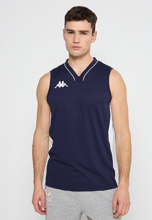 Giovane uomo che indossa una canotta sportiva blu navy senza maniche con pannelli laterali bianchi e pantaloni della tuta grigi, in piedi davanti a uno sfondo semplice.