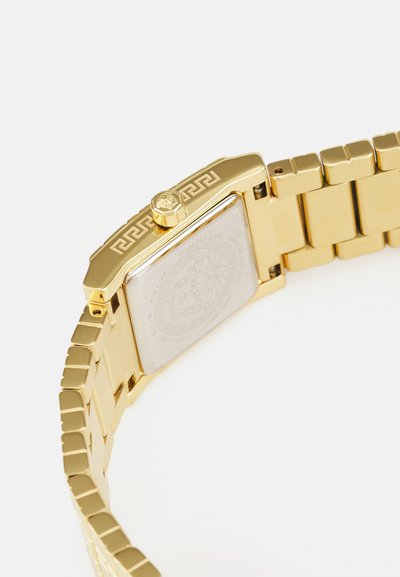 Gold-tone stainless steel watch with a rectangular case, patterned bracelet, crown detail, and a smooth, light-colored back.