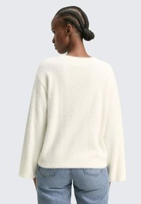 Weißer, flauschiger Pullover mit weicher Textur, weiten Ärmeln und rundem Ausschnitt, kombiniert mit hellblauen Jeans.