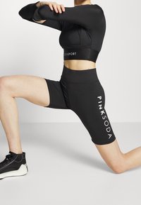 Czarny sportowy strój składający się z krótkiego topu i szortów z wysokim stanem. Materiał jest gładki, z białym napisem "PINKSODA" po boku.