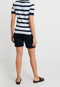 Granatowo-biały top w paski z krótkim rękawem, zestawiony z granatowymi szortami; tkanina o fakturze z podwiniętymi brzegami, noszony z czarnymi klapkami.
