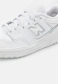 Weißer sportlicher Sneaker mit einem glatten Leder-Obermaterial, tonalen Schnürsenkeln, gepolsterter Knöchelpartie und sichtbarem Logo-Detail an der Seite und Sohle.
