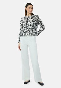 Schwarz-weiße Leopardenmuster-Bluse mit rundem Ausschnitt und langen Ärmeln, kombiniert mit weißen weit geschnittenen Hosen und schwarzen Ballerinas.