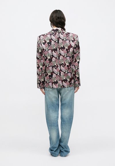 Μπουφάν με ανθικό μοτίβο πάνω σε σκούρο φόντο, ραμμένο κομψά με φαρδιές πέτσες γιακά· συνδυασμένο με ανοιχτόχρωμα, άνετα τζιν παντελόνια σε χαλαρή γραμμή.