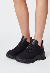 Czarne sneakersy z teksturowanym wierzchem z materiału, skórzanymi akcentami i kontrastującymi kremowymi sznurowadłami. Masywna czarna gumowa podeszwa.