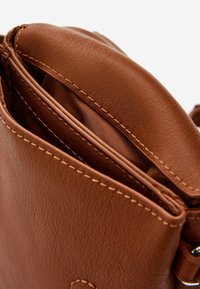 Brązowa skórzana torebka o teksturowanym wykończeniu, z wieloma wewnętrznymi przegródkami i kontrastowym wykończeniem szwów. Miękka, strukturalna konstrukcja.